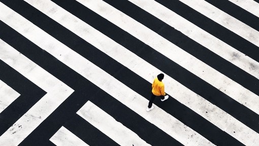 Person in yellow jumper crossing black and white striped road