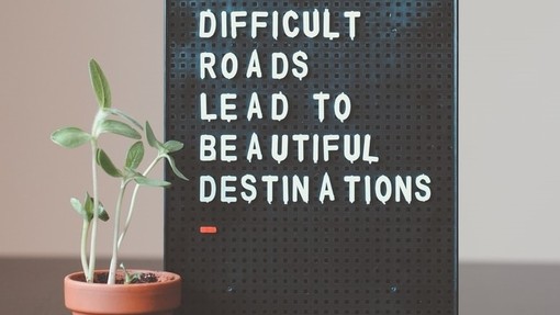 Sign reading Difficult roads lead to beautiful destinations with a plant next to it