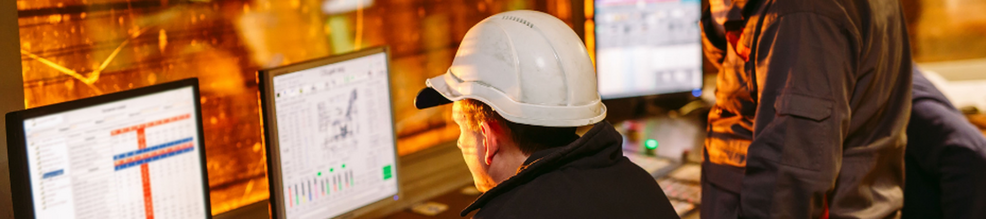 Engineers in hard hats looking at data on computer screens