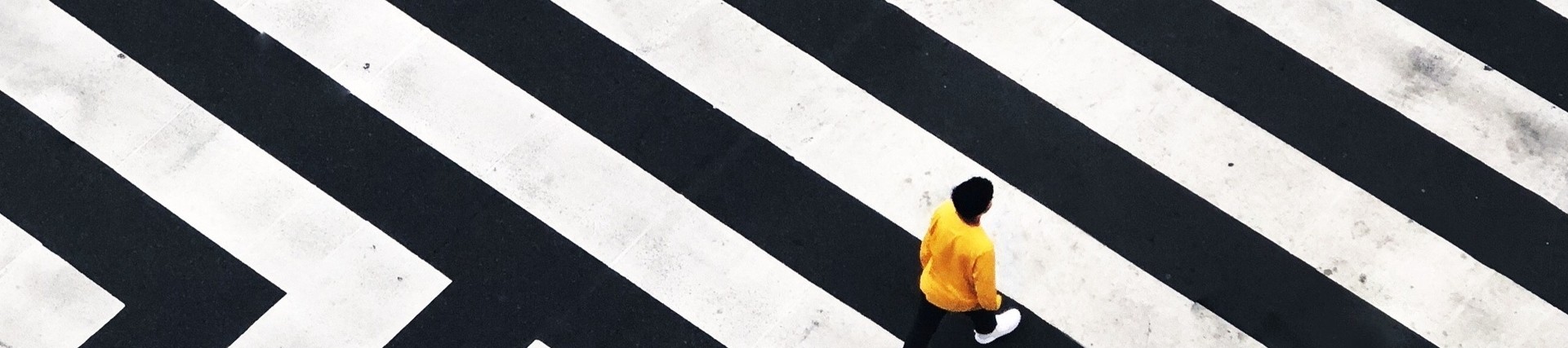 Person in yellow jumper crossing black and white striped road